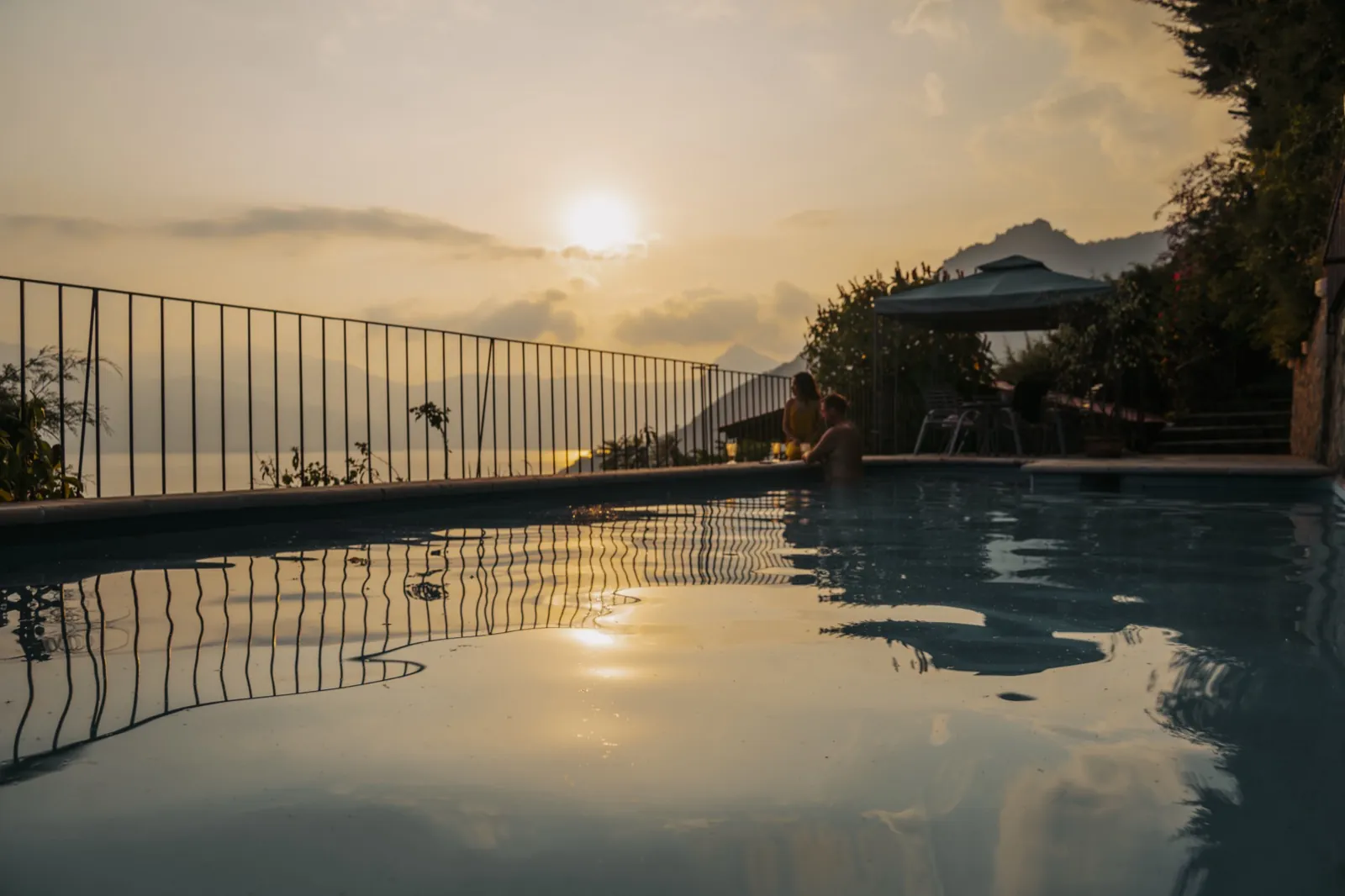 Loma de Atitlan pool at golden hour with volcano silhouette and sunset reflections on the water