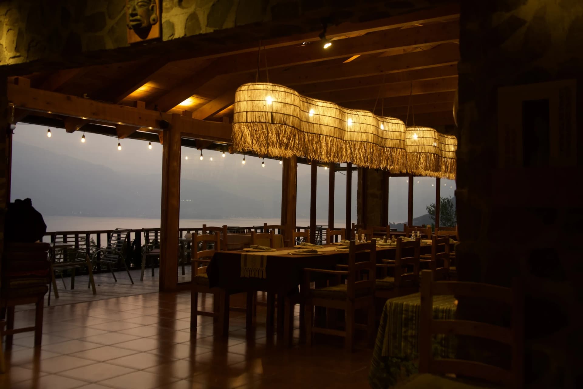 The open-air dining room at Loma de Atitlán at dusk, lamps lit over the long table, the lake beyond