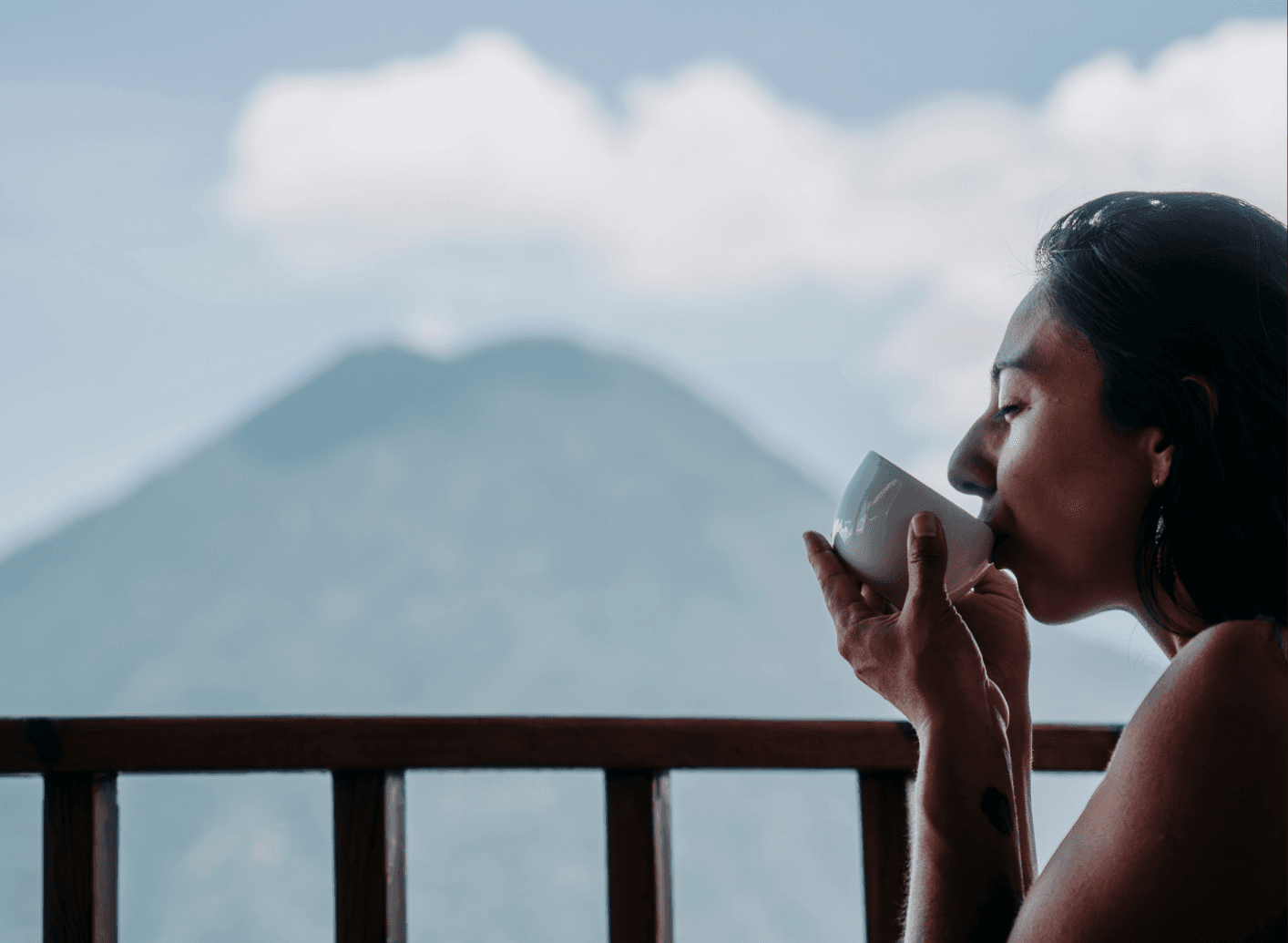 Woman sipping coffee on balcony with volcano view at Loma de Atitlan