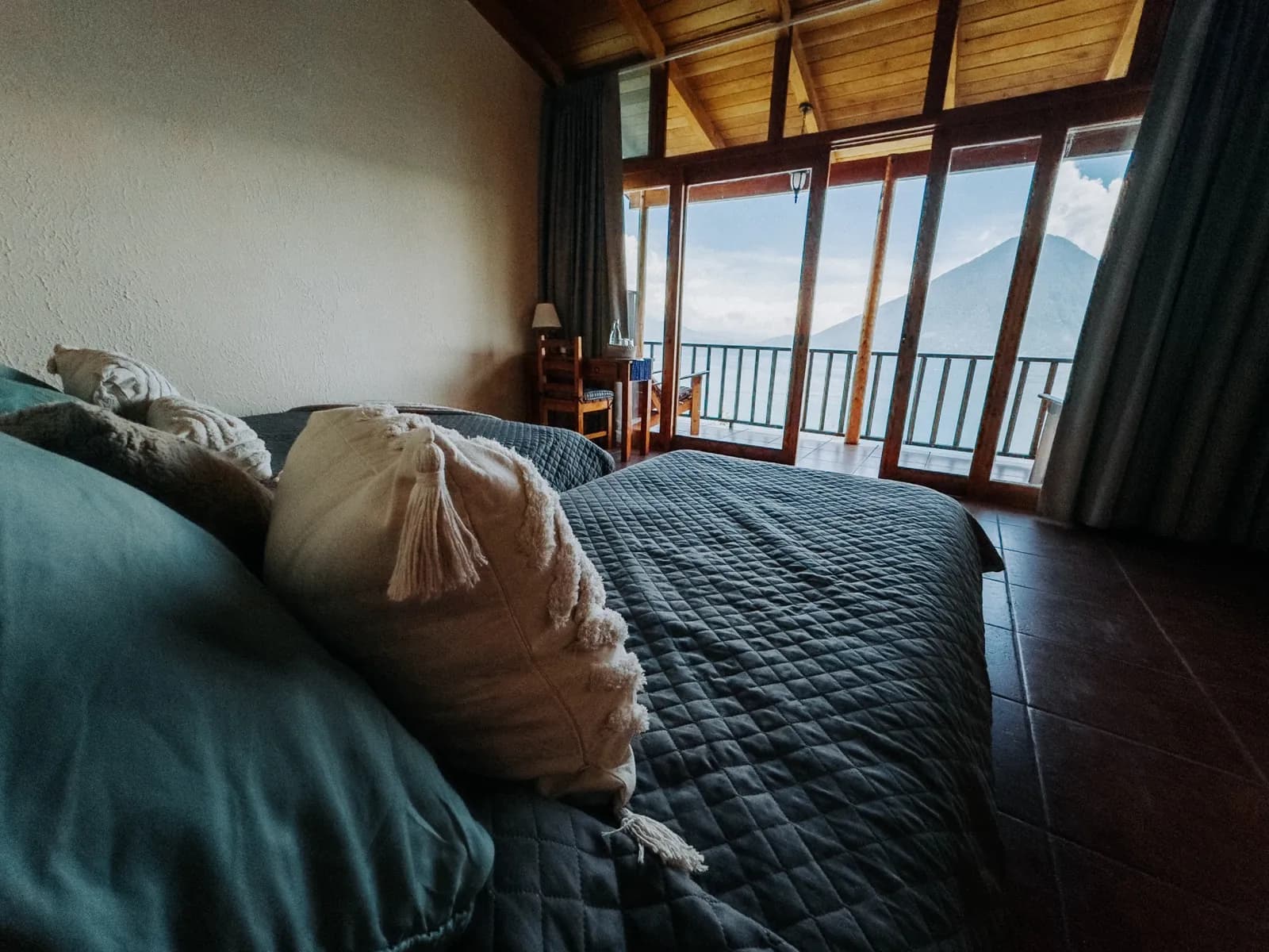 A private bungalow bedroom at Loma de Atitlán, the volcano framed in the window over Lake Atitlán